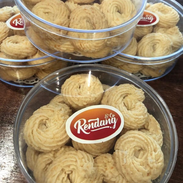 Three clear plastic containers filled with light-colored, spiral-shaped Rendang & Co. cookies.