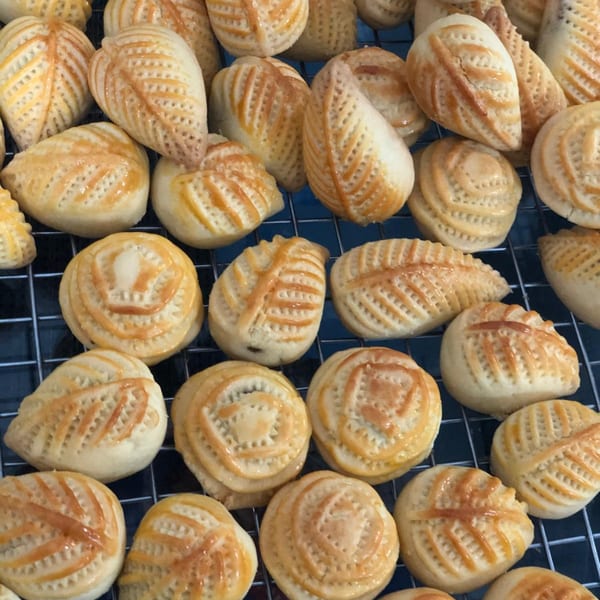 A close-up of various golden-brown Indonesian pastries with intricate patterns on a cooling rack.