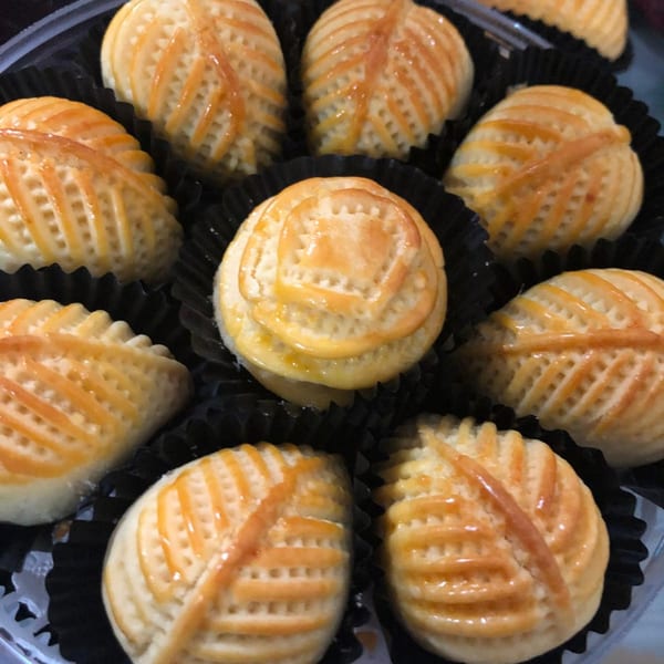 A close-up of several small, golden-brown Indonesian pineapple tarts (Nastar) in black paper cups.