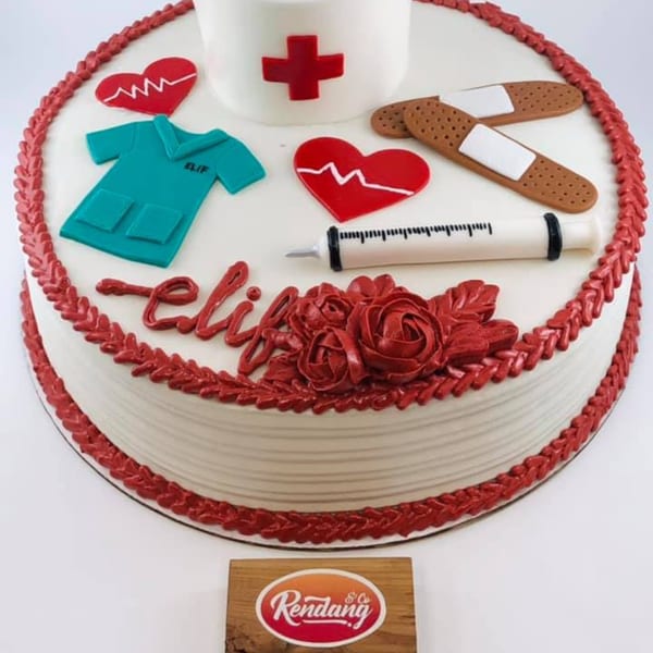 White cake decorated with red icing, nurse's cap, scrubs, hearts, bandages, and a syringe.