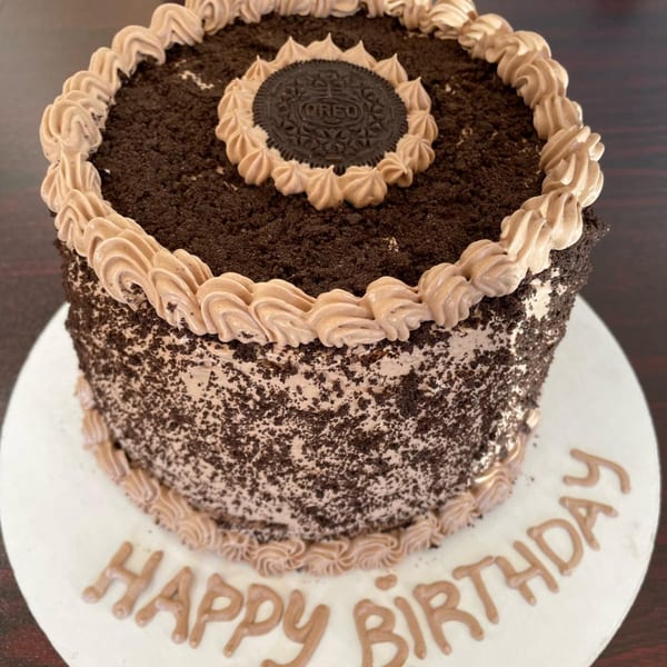Chocolate birthday cake with cookie crumbles, an Oreo, and "Happy Birthday" written in frosting.