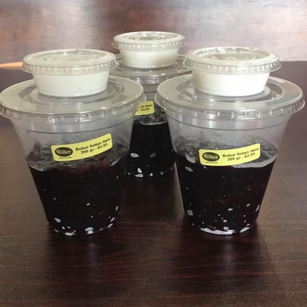 Three plastic cups of Bubur Ketan Item, an Indonesian black glutinous rice porridge, with cream on top.
