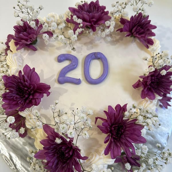 White cake with purple "20" and decorated with purple chrysanthemums and baby's breath.