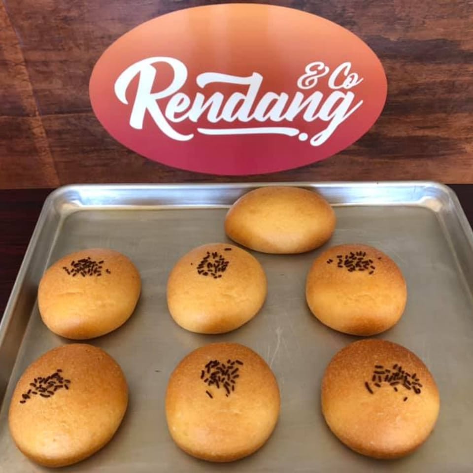 Seven golden-brown buns with chocolate sprinkles on a metal tray, with the Rendang & Co logo in the background.