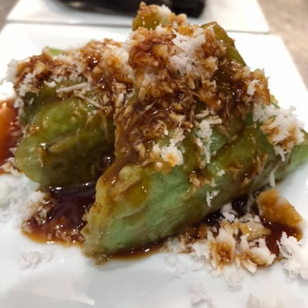 Green Indonesian dessert with brown sauce and shredded coconut on a white plate.