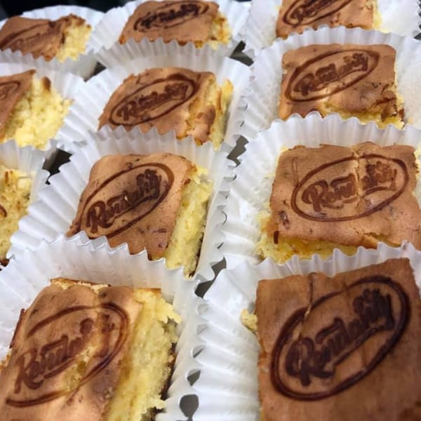 Rows of square Rendang & Co. cakes with a branded logo, in white paper liners.