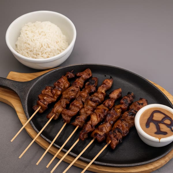 Indonesian chicken satay skewers with peanut sauce and a bowl of white rice on a wooden board.