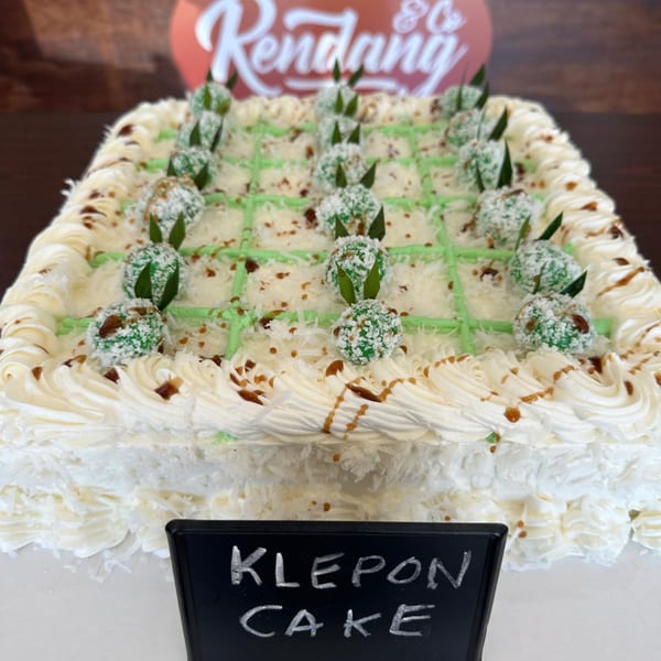 A square Klepon cake from RENDANG & CO, topped with green klepon balls, white frosting, and caramel drizzle.