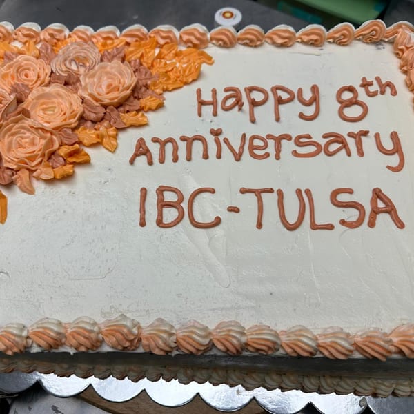 White anniversary cake with orange frosting roses and "Happy 8th anniversary IBC-TULSA" written on it.