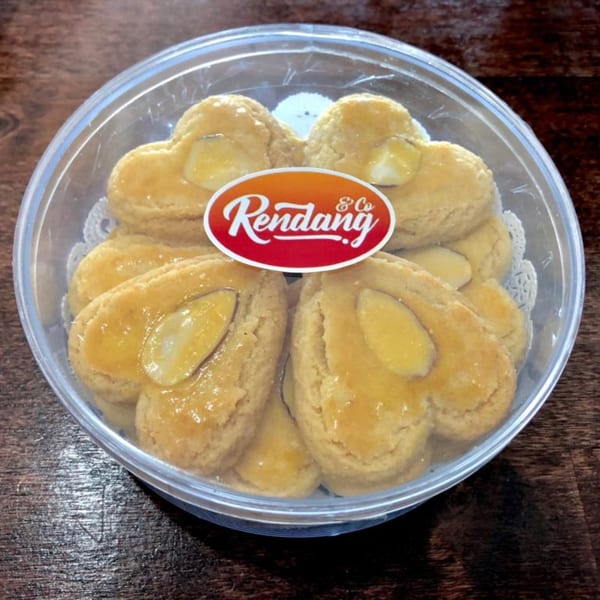Heart-shaped Rendang & Co cookies with almond slices in a clear plastic container.