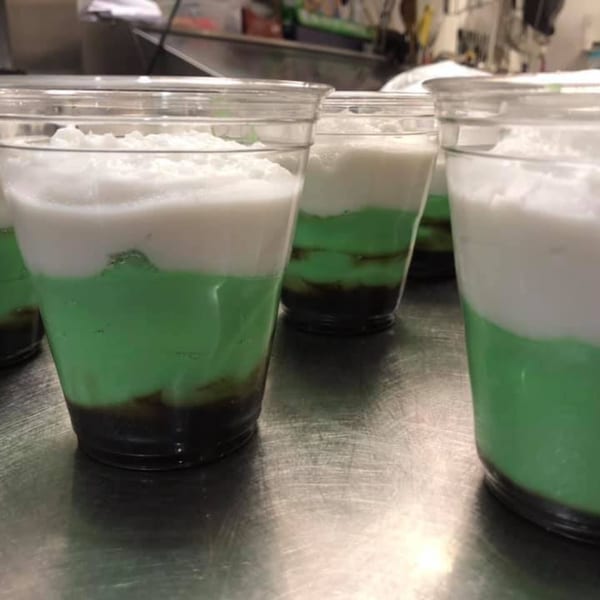 Rows of clear plastic cups filled with layered green, white, and dark brown desserts.