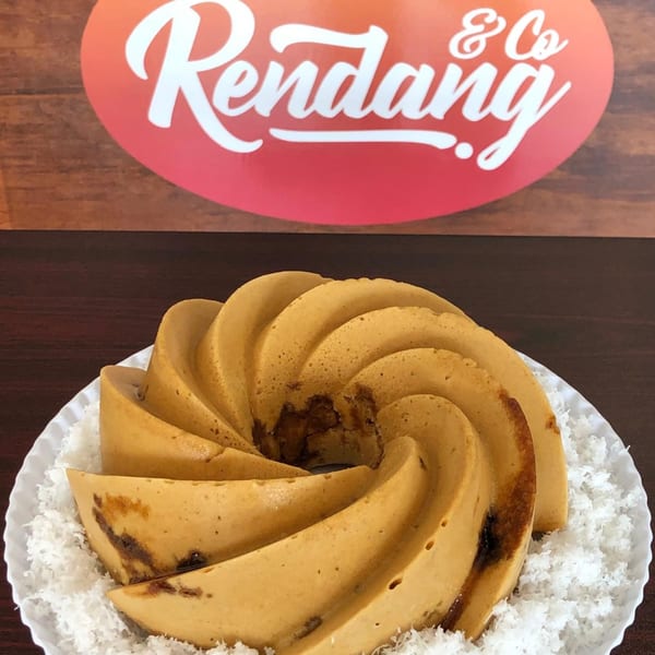 A golden-brown spiral cake with dark filling, surrounded by shredded coconut on a white plate.