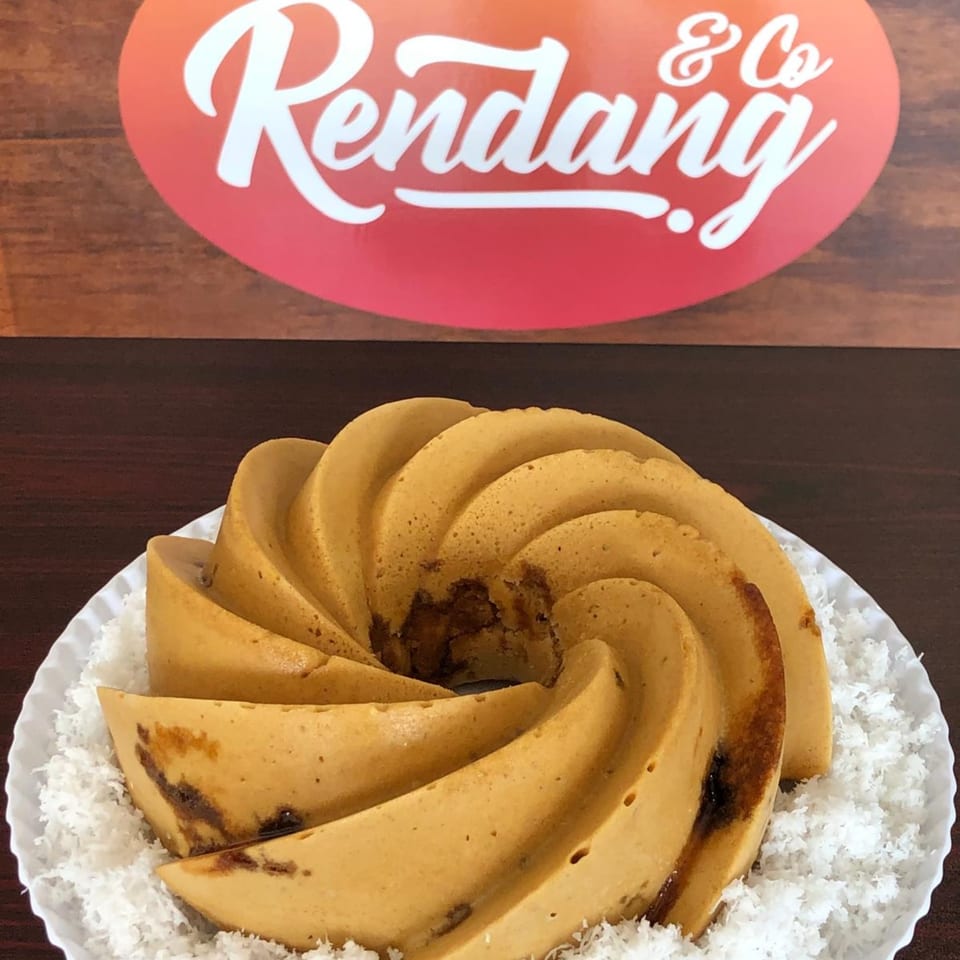 A golden-brown spiral cake with dark filling, surrounded by shredded coconut on a white plate.