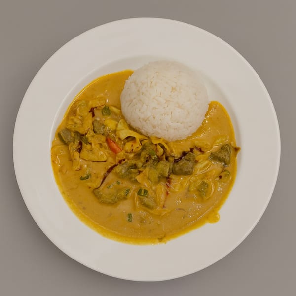 Indonesian chicken curry with vegetables and a scoop of white rice on a white plate.