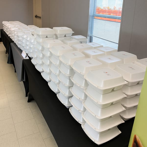 Long tables covered in black cloths, stacked with numerous white takeout containers for catering.