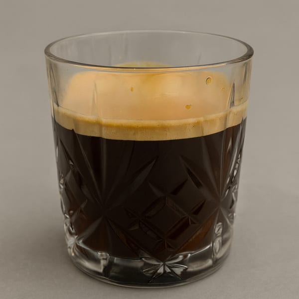 Dark espresso with a thick layer of golden crema in a textured glass.