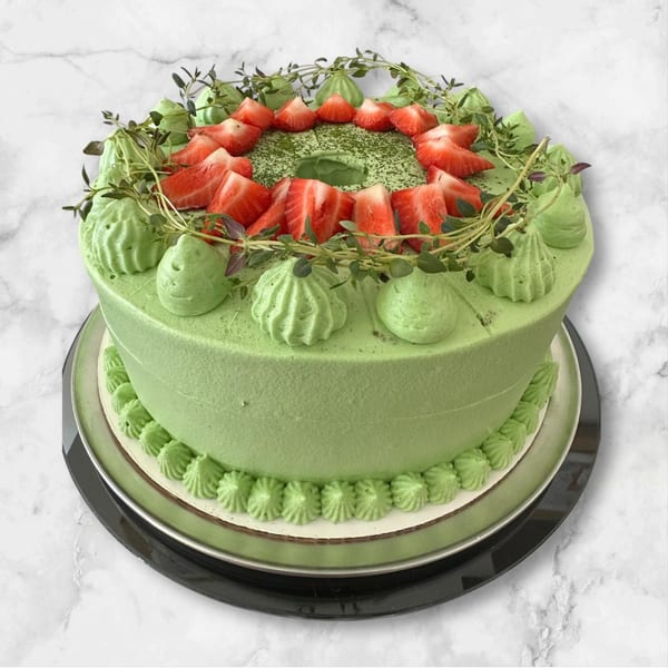 Green cake with piped frosting, topped with fresh strawberries and herbs, on a marble surface.