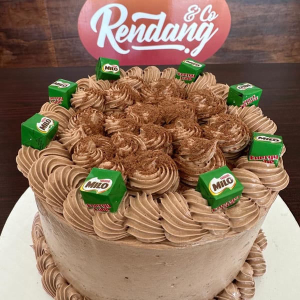Chocolate cake with Milo Energy Cube candies and cocoa powder on top, with the Rendang & Co logo.