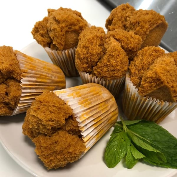 A plate of fluffy brown Indonesian steamed cakes (bolu kukus) in paper liners with mint leaves.