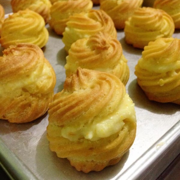 Golden-brown cream puffs with creamy filling arranged on a baking sheet.