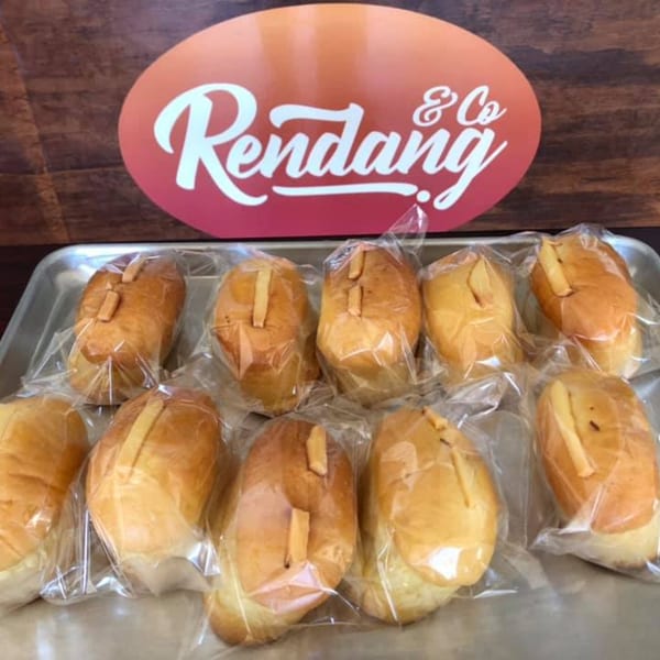 Ten individually wrapped Rendang & Co Indonesian buns with cheese on a metal tray.