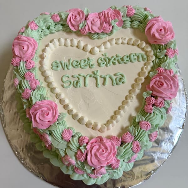 Heart-shaped cake with pink roses, green leaves, and "sweet sixteen Sarina" written in green icing.