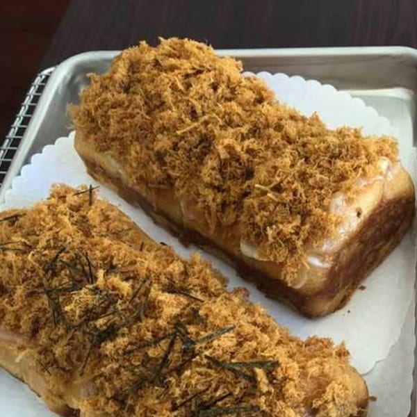 Two loaves of bread topped with shredded meat floss and dark seaweed on a metal tray.