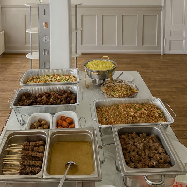 A buffet table laden with various Indonesian dishes, including satay, rice, and meat in serving trays.