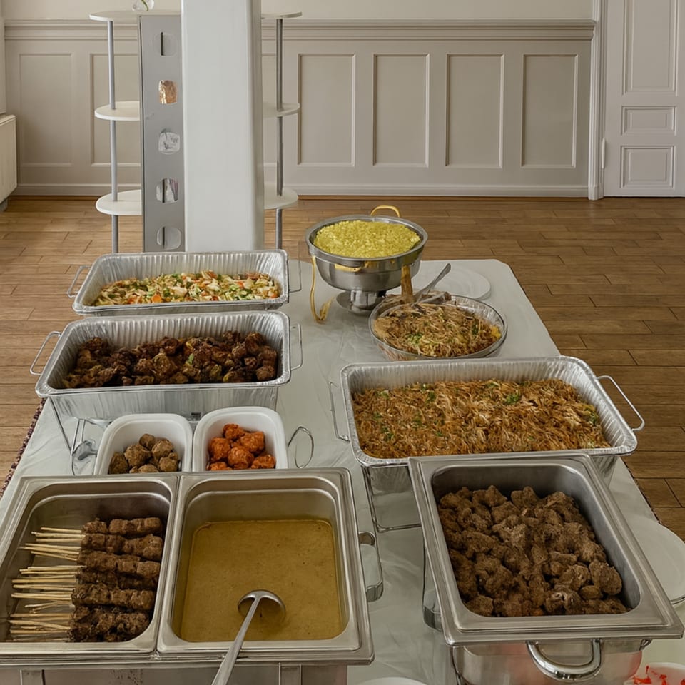 A buffet table laden with various Indonesian dishes, including satay, rice, and meat in serving trays.
