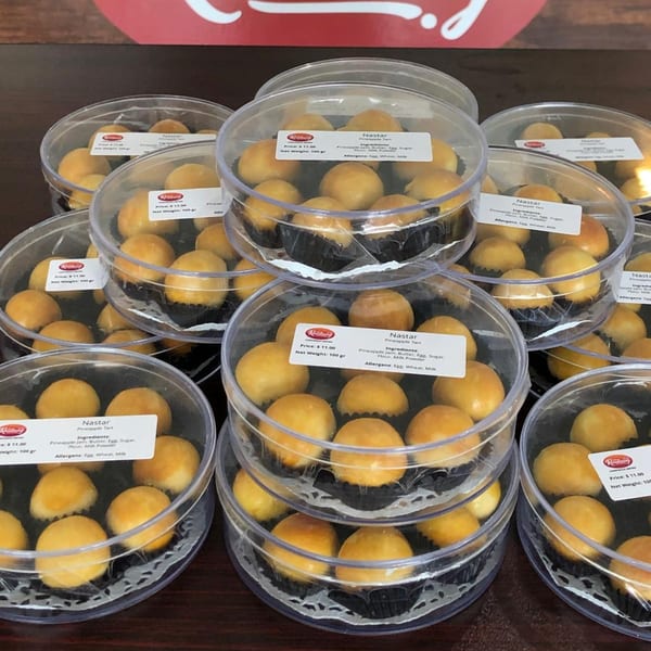 Multiple clear plastic containers filled with golden-brown Nastar pineapple tarts, stacked and arranged on a table.