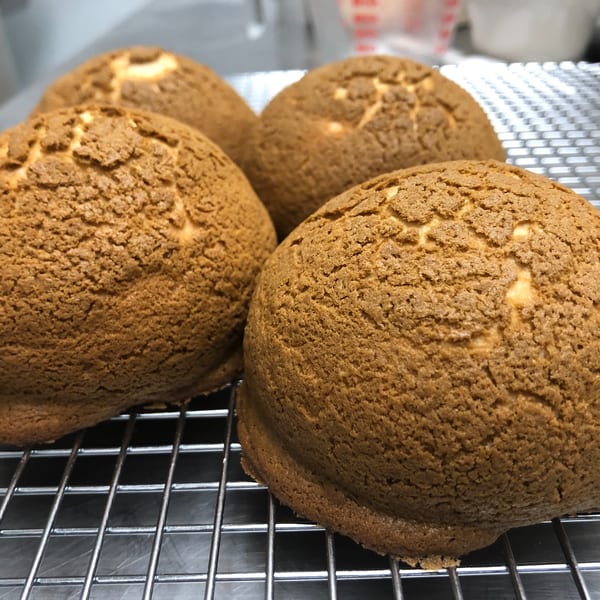 Four freshly baked, golden-brown Indonesian coffee buns with textured tops cooling on a wire rack.