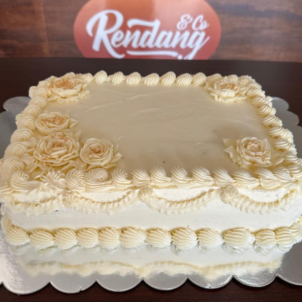 A rectangular white cake with intricate frosting roses and gold sprinkles, on a silver scalloped tray.